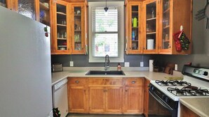 Une cuisine avec des meubles de rangement en bois, un évier, une cuisinière et une fenêtre avec des stores.