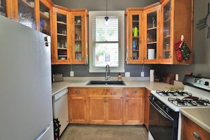 A kitchen with wooden cabinets, a sink, a stove, and a window with blinds. - Barrio Viejo, Charming Historic Downtown Home (Tucson)