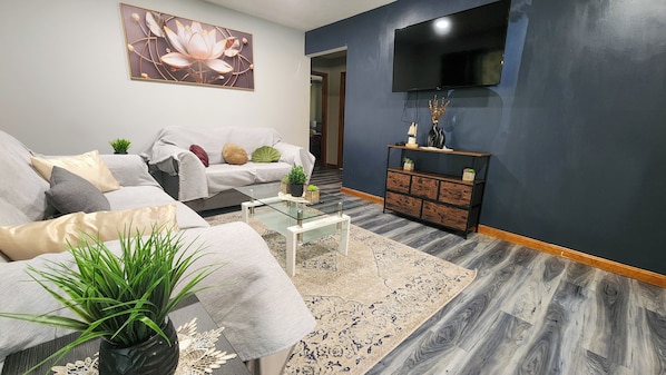 A living room with a sofa, coffee table, and a flat-screen TV mounted on the wall.