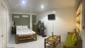 Un dormitorio con cama, mesita de noche, ventilador, televisor y ventana con persianas.
