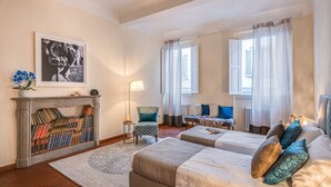 A bedroom with two beds, a fireplace, a chair, and a table.
