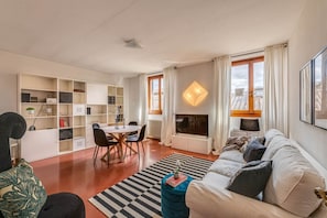 A living room with a sofa, a dining table, chairs, a bookshelf, a fireplace, and large windows. - Apartments Florence Accademia Charme (Firenze)
