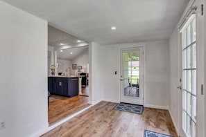 Un pasillo con suelo de madera que conduce a una zona de cocina con armarios oscuros y una puerta blanca.