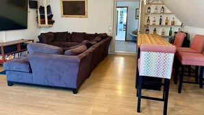 Ein Wohnzimmer mit Ecksofa, Fernseher, Couchtisch aus Holz und einer Bar mit Flaschen.