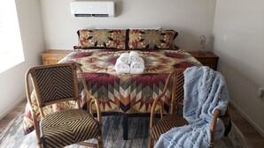 A bedroom with a large bed, two chairs, a bedside table, and an air conditioning unit.
