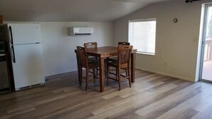 A dining area with a wooden table and chairs, a white refrigerator, and a window with blinds.