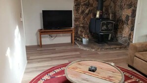 A living room with a stone fireplace, a television on a stand, and a round coffee table.