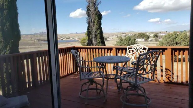 A wooden deck with a table and chairs, overlooking a landscape with trees and distant buildings.