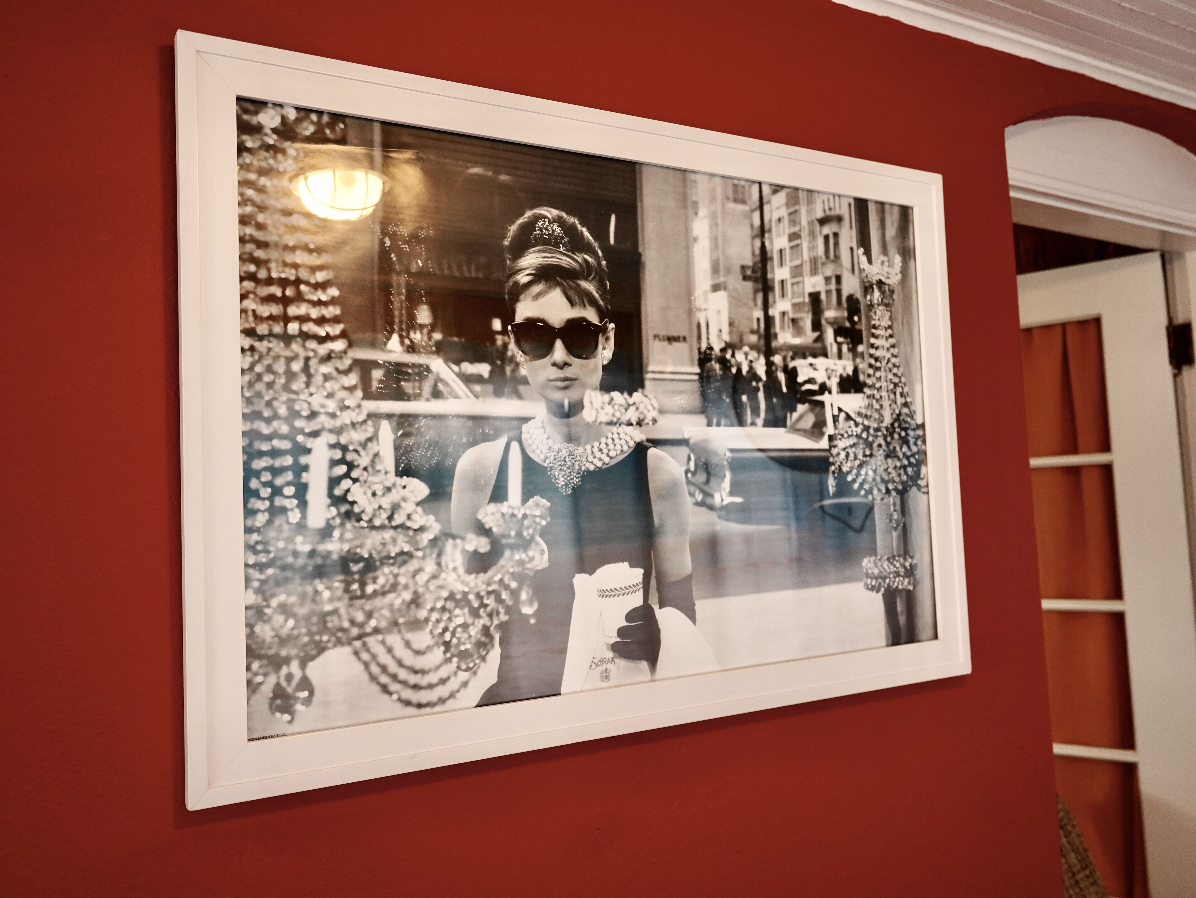 Een ingelijste foto van een persoon in een nette jurk met een ketting, voor een rode muur.