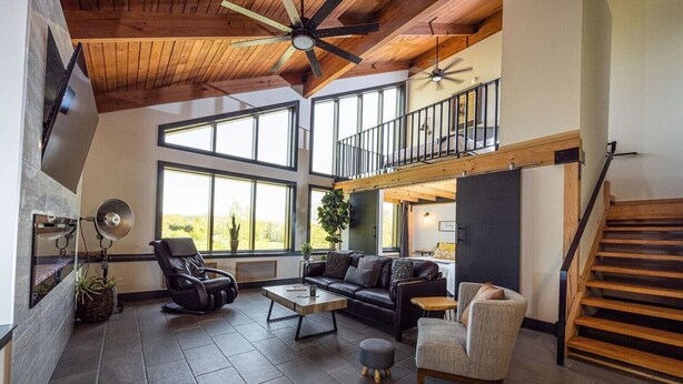 Un amplio salón con techo alto, ventanas grandes, chimenea y una escalera que sube a un nivel superior.