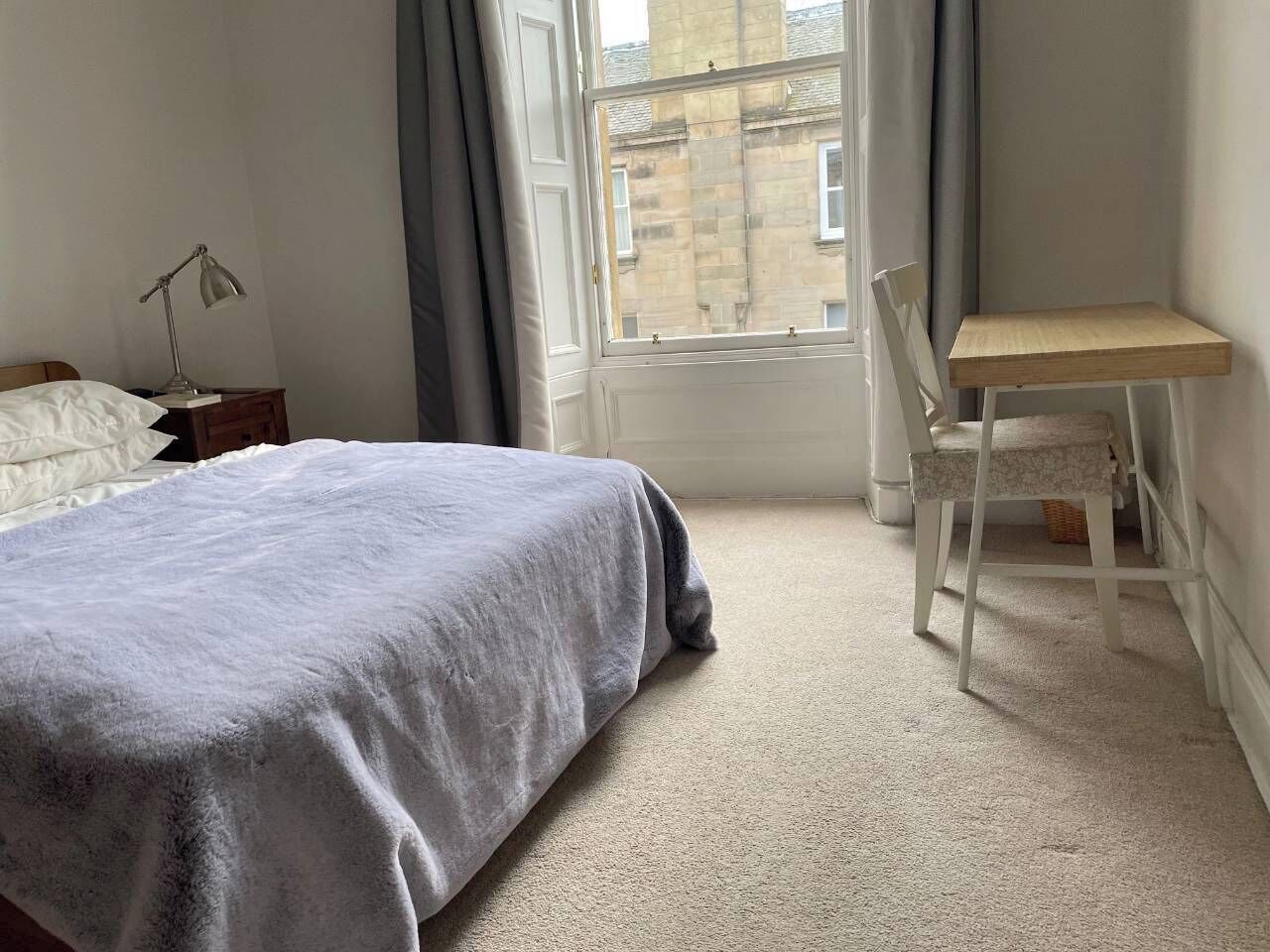 A bedroom with a bed, a desk, and a window.