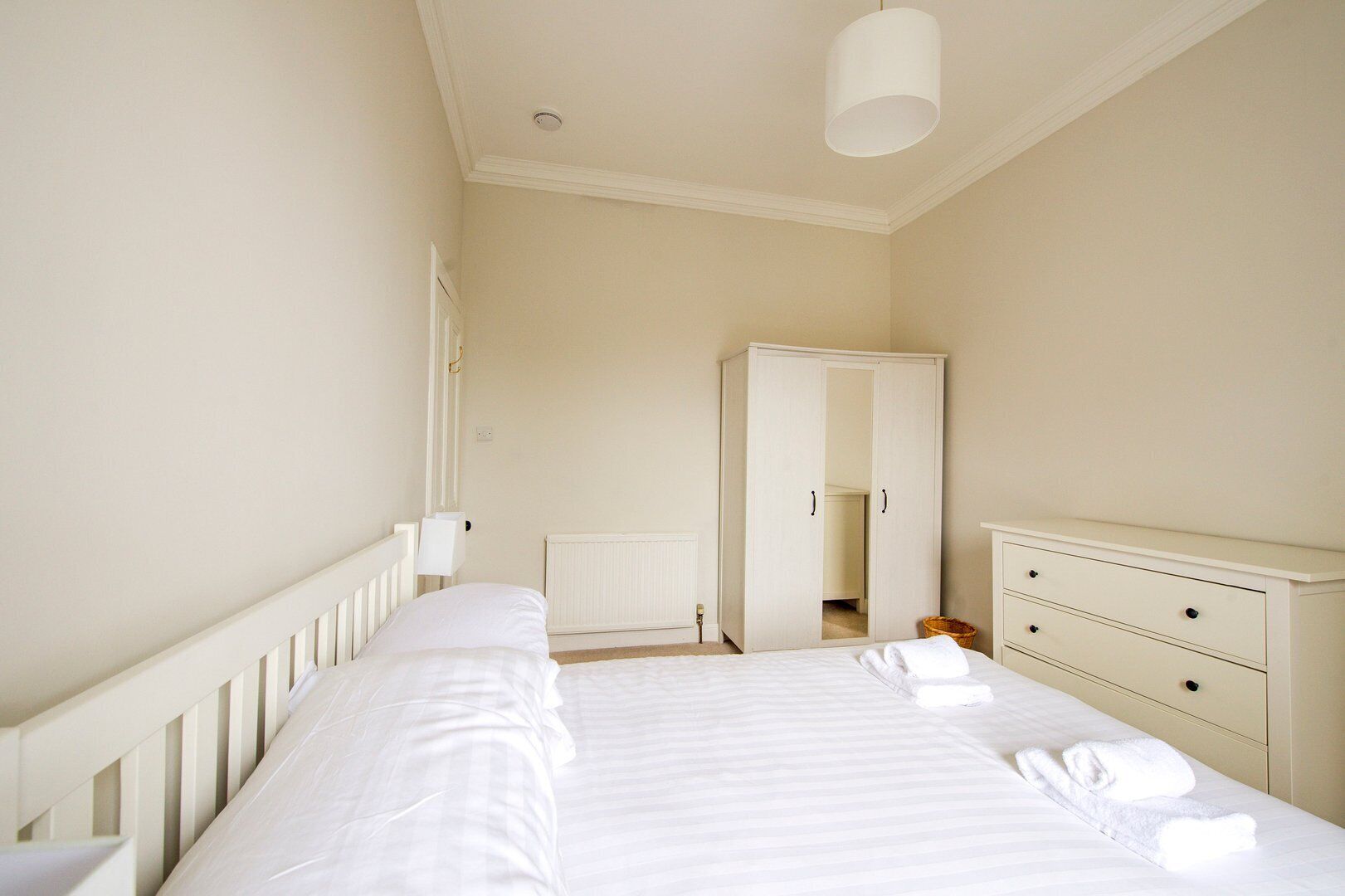 A bedroom with a bed, a dresser, a wardrobe, and a radiator.