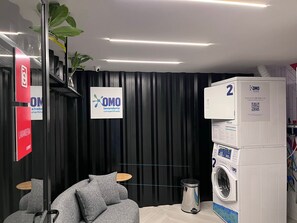 A modern laundry room with a black wall, a grey sofa, a washing machine, and a sign for OMO laundry services.