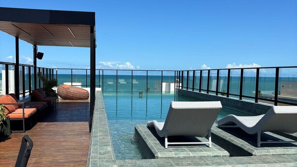 An infinity pool with lounge chairs, a covered seating area, and a view of the ocean. - Flat Gold Get One - João Pessoa (João Pessoa)