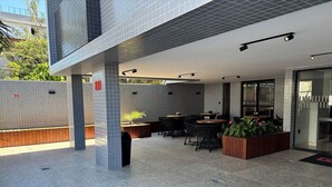 A modern outdoor seating area with tiled flooring, a wooden bench, and a planter with green plants. - Flat Gold Get One - João Pessoa (João Pessoa)