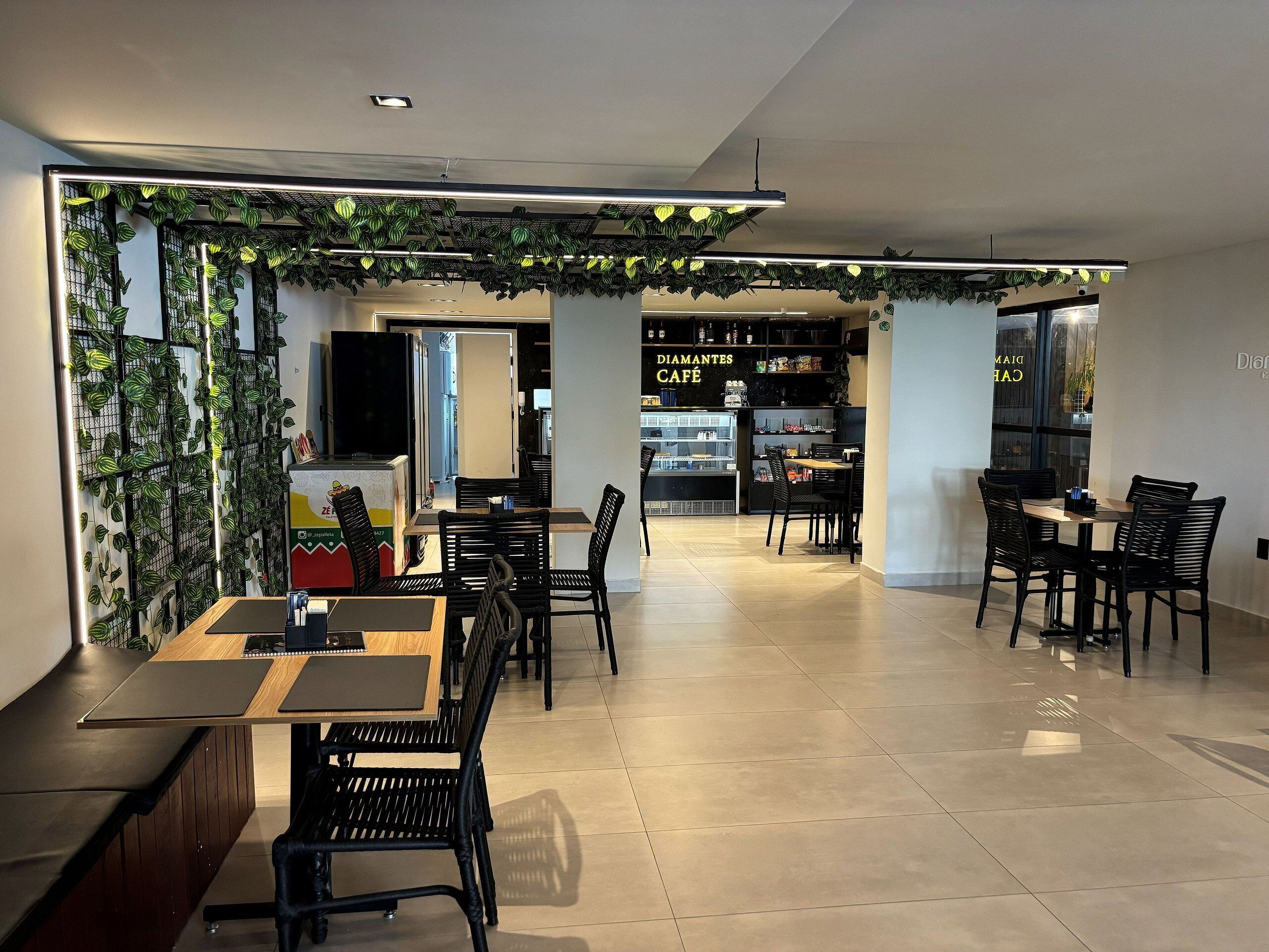 Un café moderno con mesas y sillas, una barra y una exhibición de plantas en la pared.