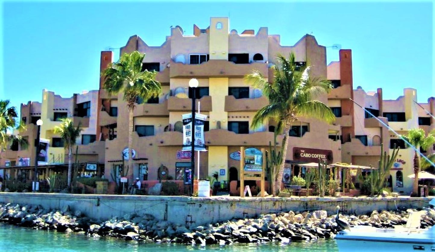 A multi-story hotel with balconies, palm trees, and a waterfront view.