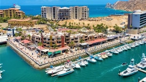 A marina with multiple boats docked, a beachfront promenade, and several multi-story buildings with balconies overlooking the water. - New Remodel / Spanish Chic Suite on the Cabo Marina (Cabo San Lucas)