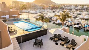 A rooftop pool area with lounge chairs and a table, overlooking a marina with boats and a mountainous backdrop. - New Remodel / Spanish Chic Suite on the Cabo Marina (Cabo San Lucas)