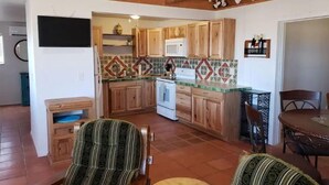 Eine kompakte Küche mit Holzausbau, einer Mikrowelle und einer gefliesten Spritzschutzwand. Es gibt einen Essbereich mit Tisch und Stühlen sowie eine kleine Sitzecke mit gepolsterten Sitzbänken.