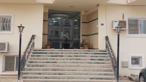A building entrance with a staircase leading to a glass door, potted plants, and air conditioning units. - Cozy / Comfy Studio (Hurghada)