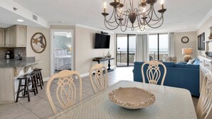 A modern living room with a dining area, a kitchen, and a balcony with a view. - Phoenix VII 203 | Orange Beach, AL (Orange Beach)