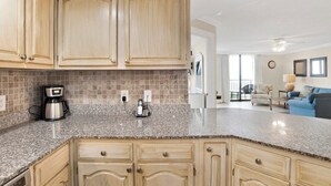 A kitchen with granite countertops, wooden cabinets, and a coffee maker. - Phoenix VII 203 | Orange Beach, AL (Orange Beach)