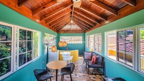 Una sala de estar con ventanales, techo de madera, zona de descanso con mesa y sillas, y vistas al exterior.