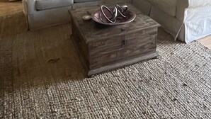 Ein Wohnzimmer mit einer Sofagarnitur, einem Couchtisch und einer Küchenzeile im Hintergrund.