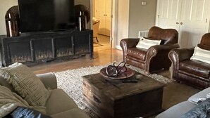 Ein Wohnzimmer mit einer Couch, zwei Sesseln, einem Couchtisch und einem Fernseher auf einem Schrank.