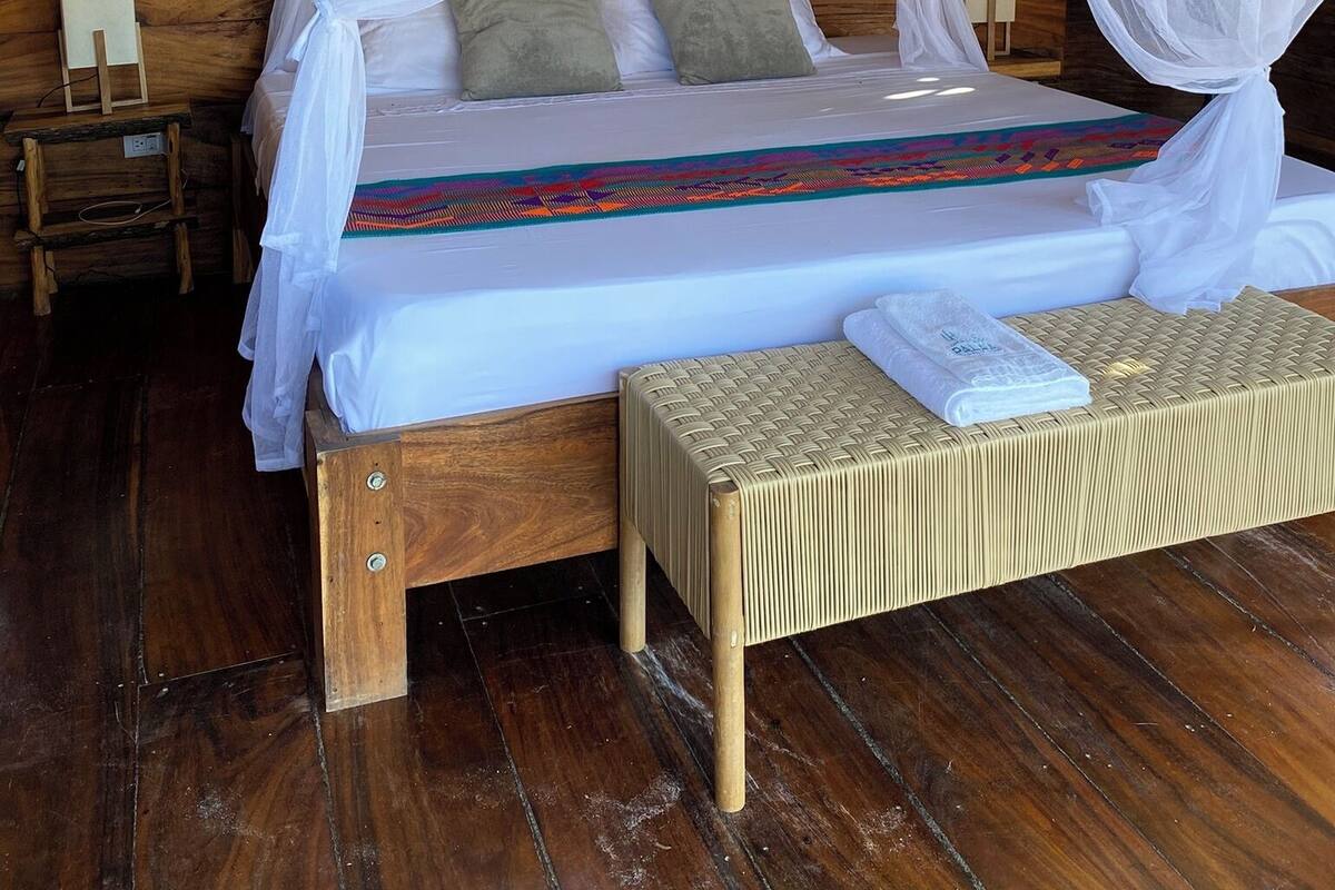 A bed with a canopy, a bedside table, and a woven bench.