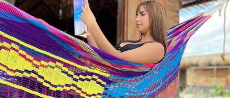 A person relaxing in a colorful hammock on a wooden deck with a thatched-roof building in the background.