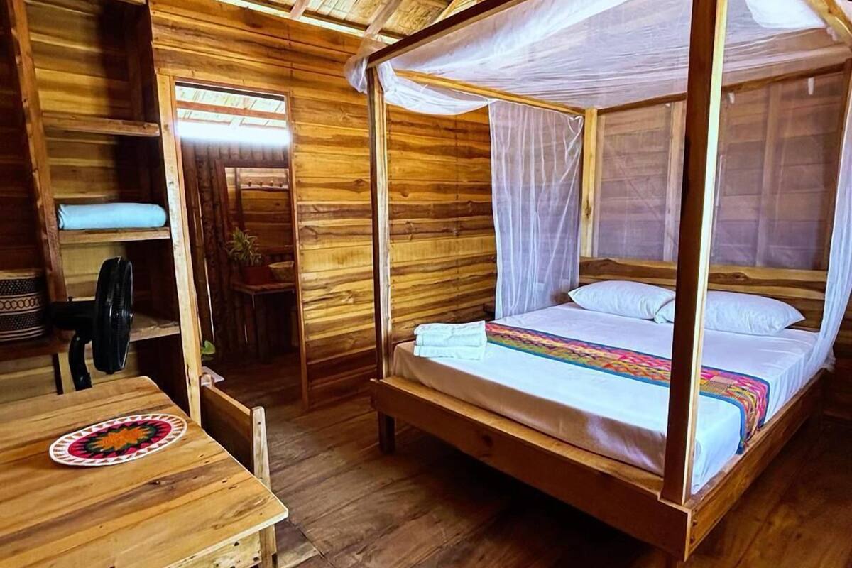 A wooden cabin with a four-poster bed, a table, and a chair.