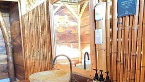 A wooden bathroom with a stone sink, bamboo walls, and a sign promoting water conservation.