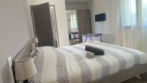Un dormitorio con cama, lámpara de noche, televisor y ventana con cortinas.