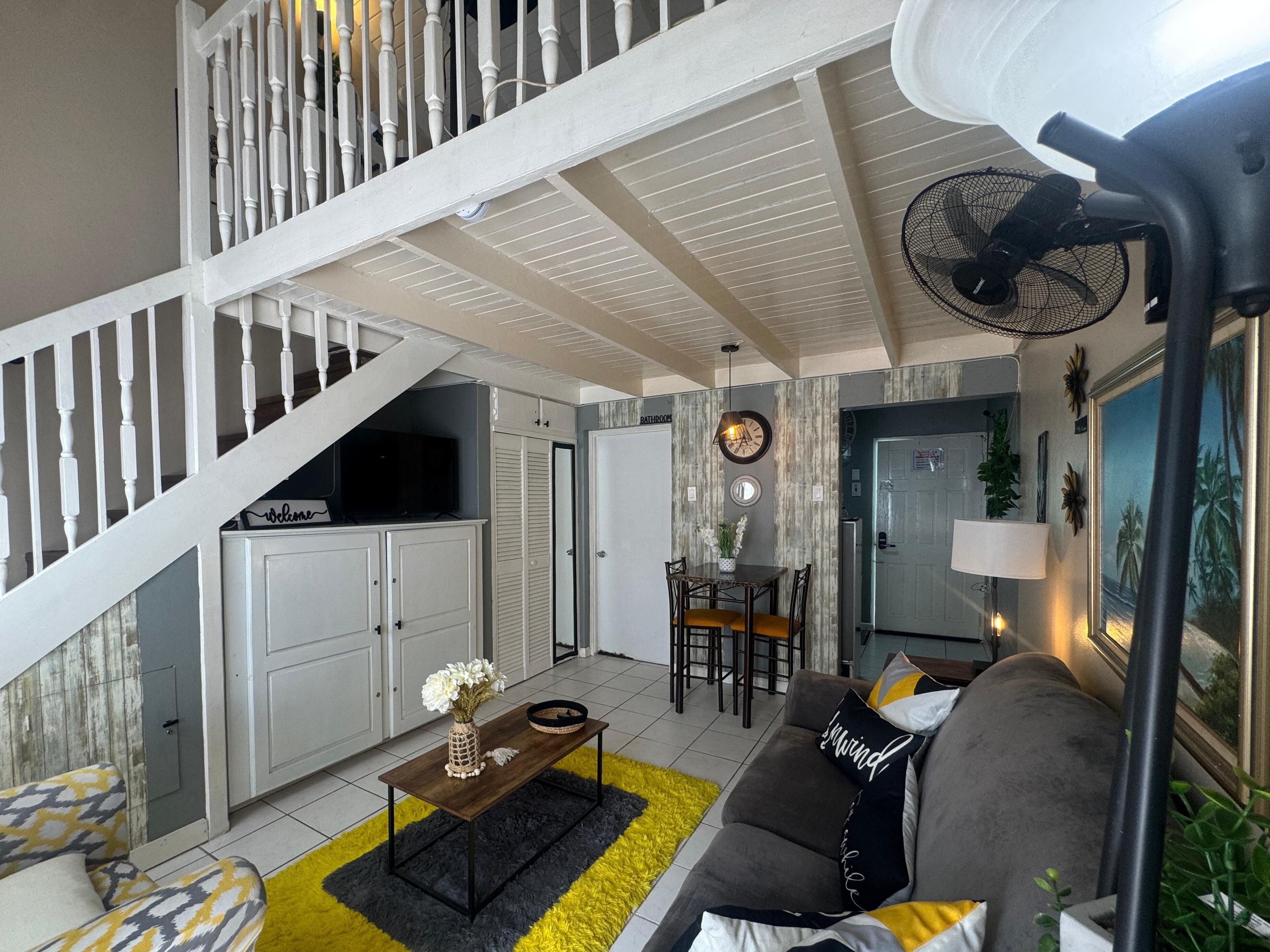 Un grand espace de vie comprenant un escalier, une table à manger avec des chaises, un canapé et un ventilateur.