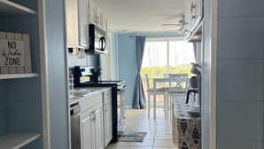A kitchen with white cabinets, a stove, and a dining area with a table and chairs. - Seaside Sunsets, Our Oceanfront Home In Aripeka (Spring Hill)