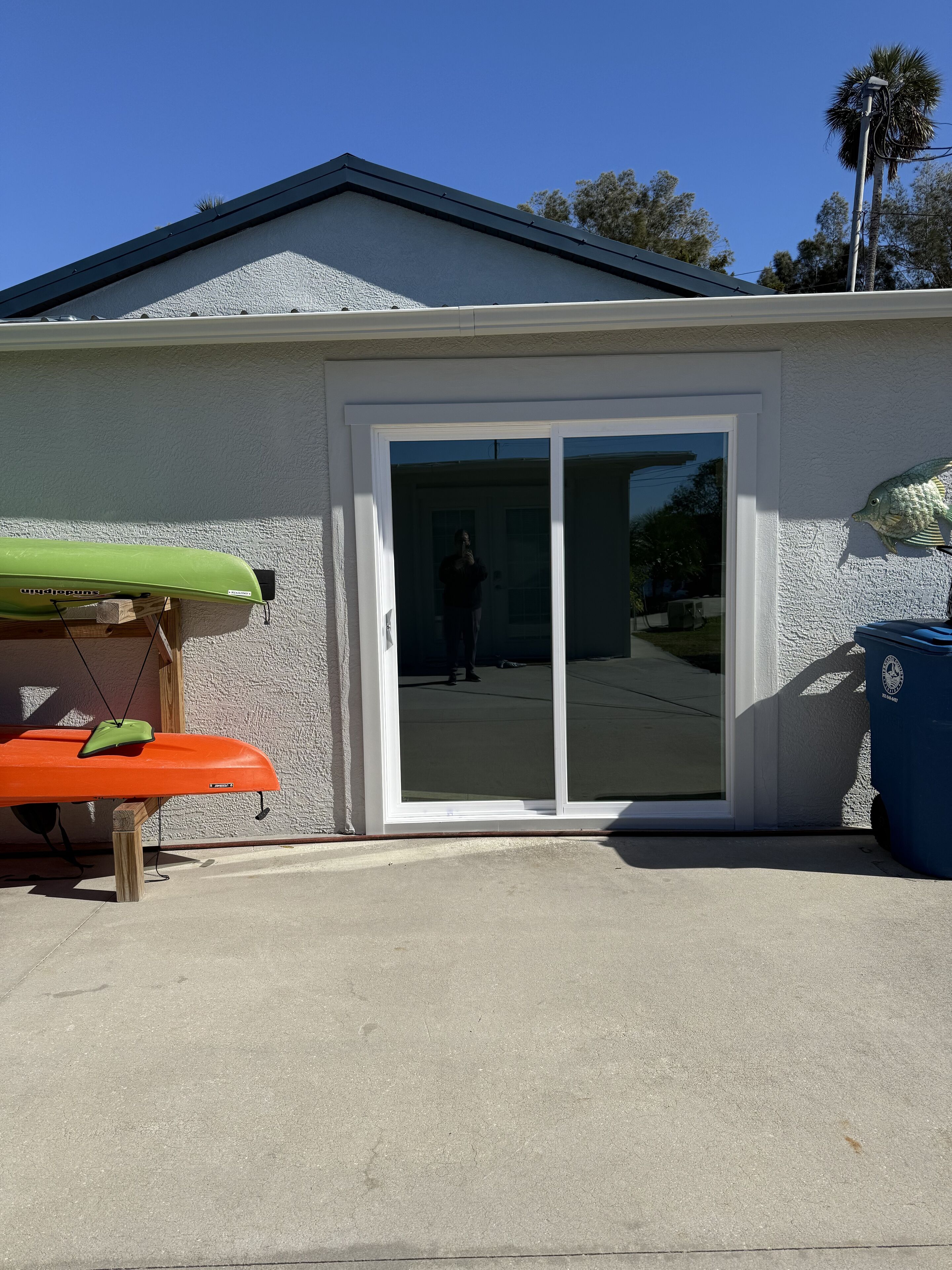 A house with a sliding glass door, a green kayak, and a blue trash bin.
