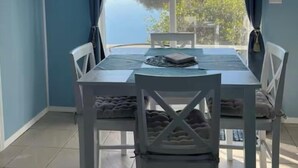 A dining area with a table and chairs, a ceiling fan, and a view of a body of water and greenery. - Seaside Sunsets, Our Oceanfront Home In Aripeka (Spring Hill)