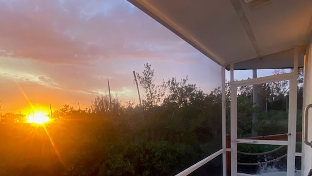 A balcony with a view of the sunset over a body of water, a chair, and a small table. - Seaside Sunsets, Our Oceanfront Home In Aripeka (Spring Hill)