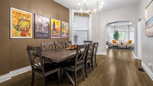 Un comedor con una mesa y sillas de madera, una araña y carteles antiguos en la pared.