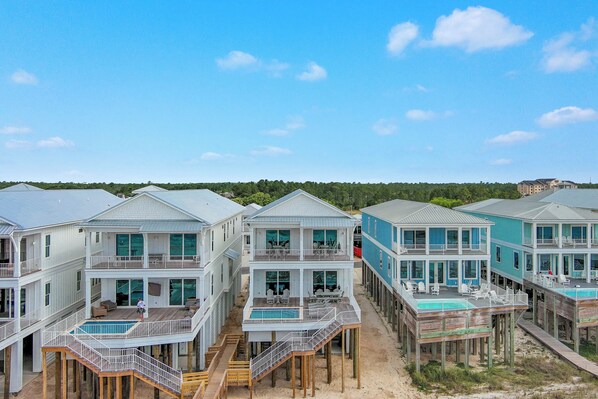 A beachfront property with multiple houses connected by walkways, featuring balconies and a swimming pool.