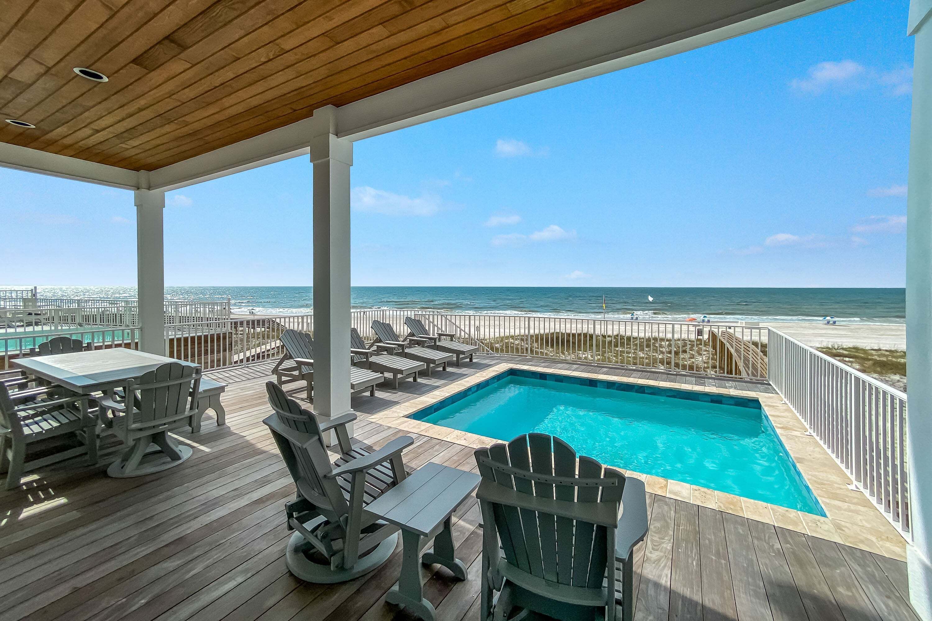 A wooden deck with a pool, lounge chairs, and a view of the ocean.