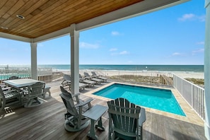 A wooden deck with a pool, lounge chairs, and a view of the ocean.