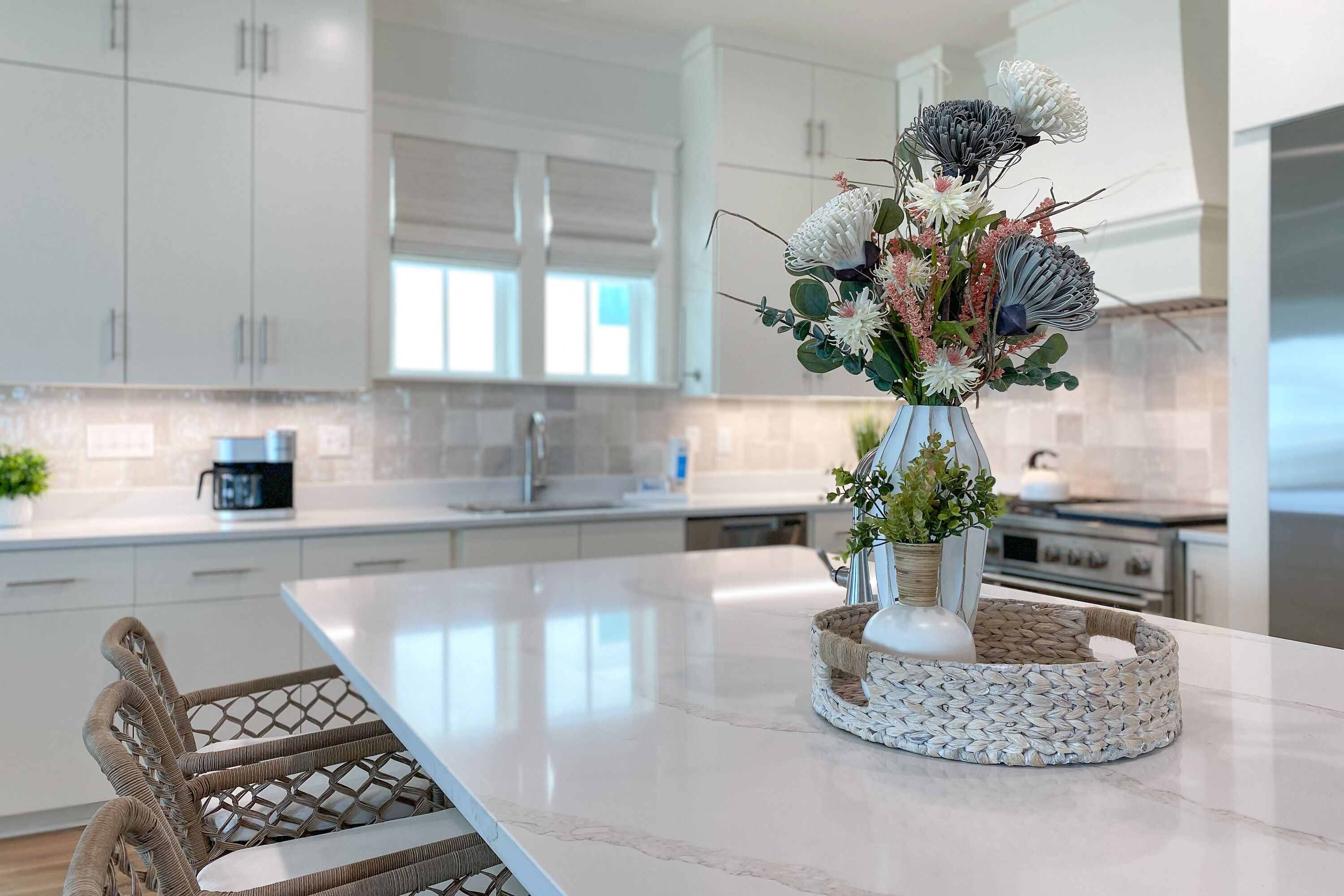 A modern kitchen with white cabinets, a marble countertop, and a woven basket centerpiece.