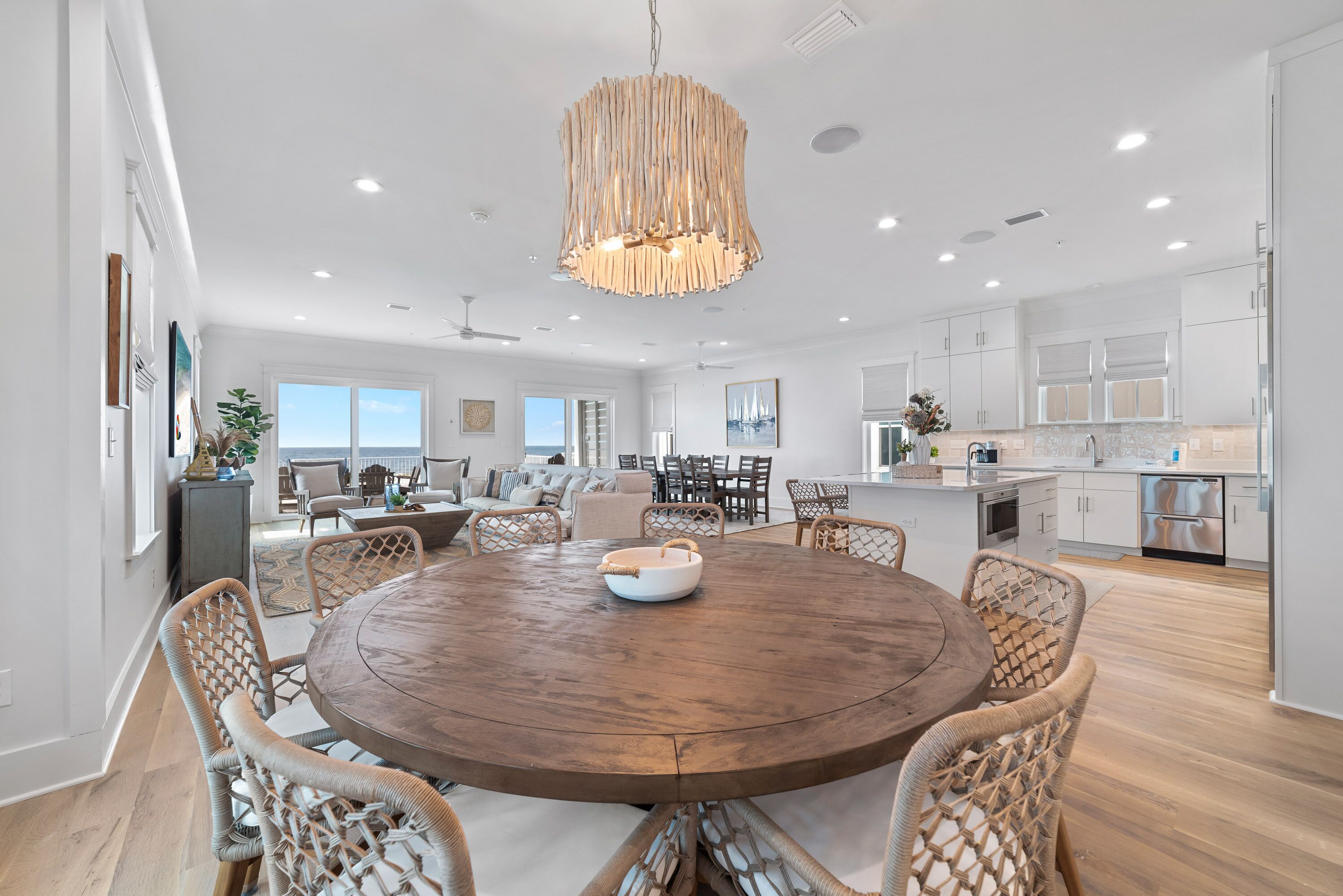 A spacious kitchen with white cabinets, a wooden dining table, wicker chairs, and a hanging light fixture.