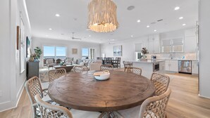 A spacious kitchen with white cabinets, a wooden dining table, wicker chairs, and a hanging light fixture. - BEACHFRONT, LUXURY HOUSE, PRIVATE POOL! (Orange Beach)