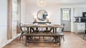A dining area with a wooden table, benches, a round mirror, and a hanging light fixture.