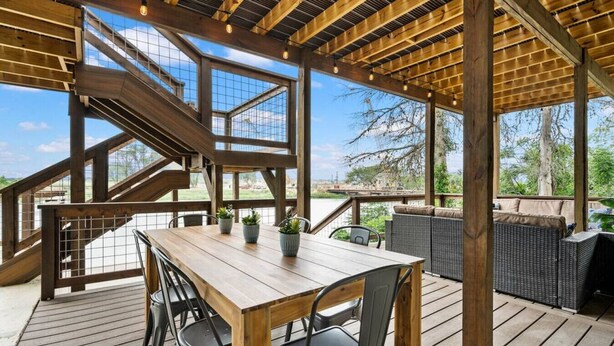 A covered outdoor area with a wooden deck, a table with chairs, and a staircase leading to an upper level.