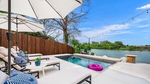 A poolside area with lounge chairs, a small pool, and a view of a lake.